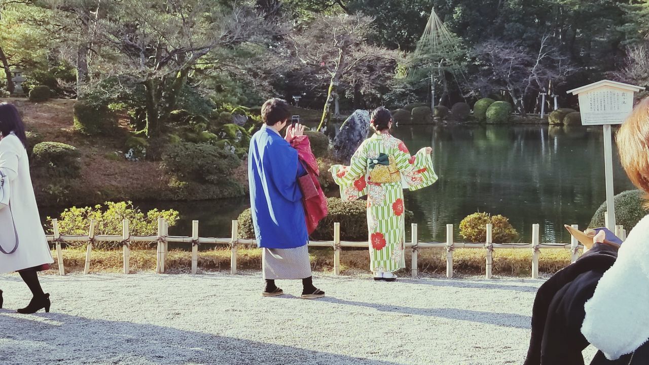 REAR VIEW OF PEOPLE STANDING BY TREE TRUNK