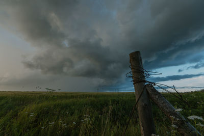 Wooden post on field against storm clouds