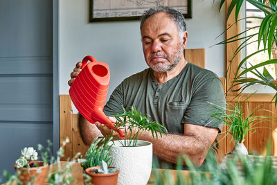 Man taking care of home flowers and succulents, planting and watering on the plants. home gardening.