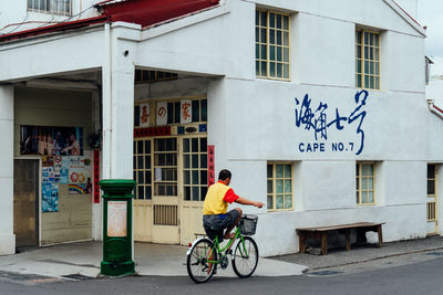 Man riding bicycle on road by building