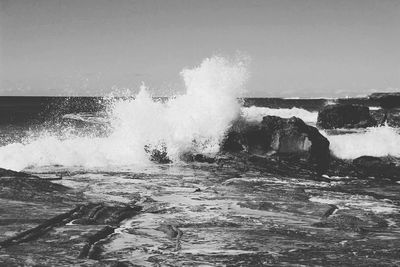 Waves splashing on rocks against sky