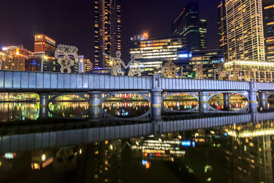 Illuminated bridge over river by buildings in city at night