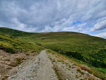 Dirt road amidst green landscape against sky