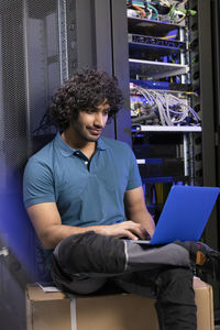 Computer programmer using laptop sitting on box in server room