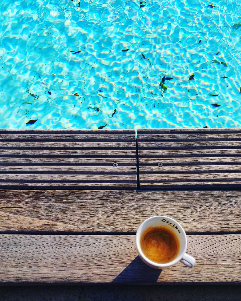 drink, refreshment, swimming pool, food and drink, pool, cup, coffee, coffee - drink, water, directly above, mug, blue, coffee cup, day, freshness, high angle view, poolside, wood - material, nature, outdoors, no people, non-alcoholic beverage, crockery