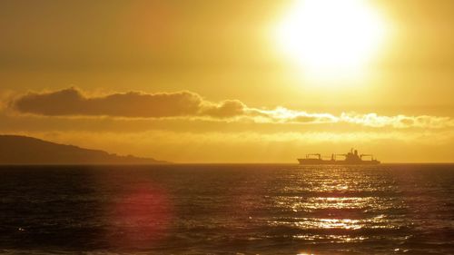 Silhouette boat sailing on sea against orange sky