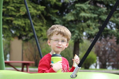 Portrait of boy winking while holding food by play equipment at park