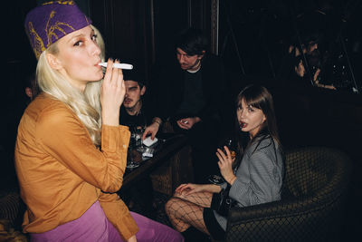 Portrait of woman smoking while sitting with friends in restaurant