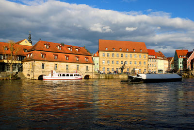 Boats moored in river by buildings in city against sky
