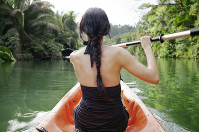 Rear view of woman kayaking on lake at forest