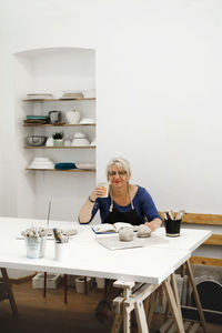 Woman potter planning work at workshop, writing in notebook in light studio her creations. clay