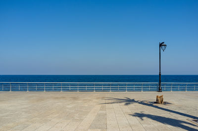 Street light by sea against clear blue sky