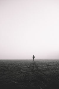 Silhouette man walking on field by sea against clear sky