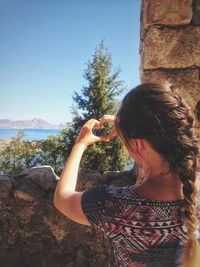 Rear view of young woman making heart shape by stone wall