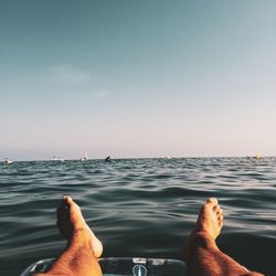 Low section of person relaxing in sea against sky