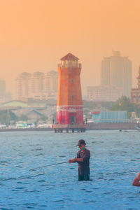 Man photographing sea against buildings in city at sunset