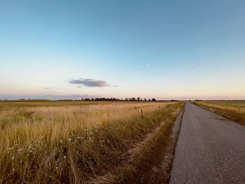 Road amidst field against sky during sunset