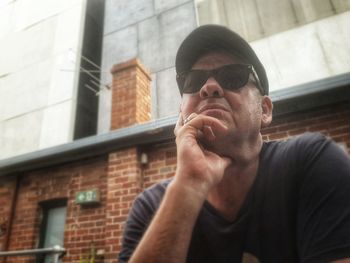 Low angle view of man wearing sunglasses while sitting against building