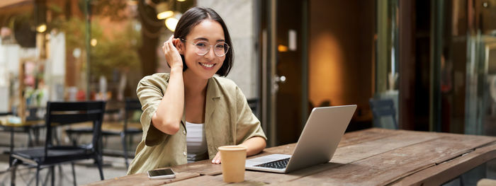 Young woman using mobile phone while sitting on table