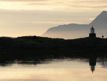 Silhouette lighthouse by lake against sky during sunset