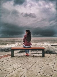 Rear view of man standing on beach against cloudy sky