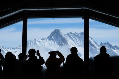 Silhouette people looking at snowcapped mountain through window