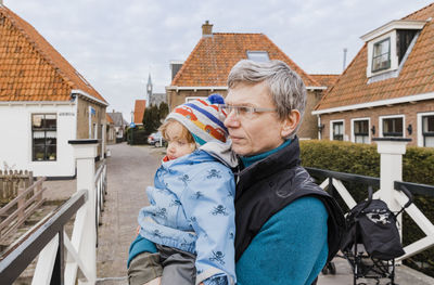 Grandfather carrying granddaughter while standing against houses