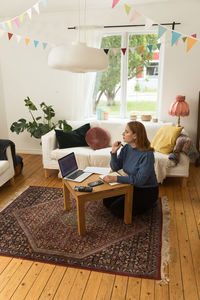 Side view of focused female radio host with mic and headphones writing in notepad while preparing for recording podcast at home