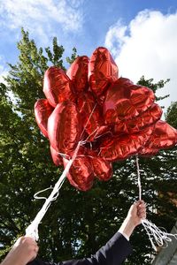 Low angle view of hand holding balloons against sky