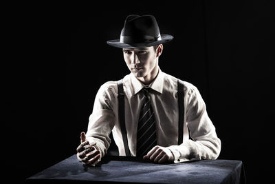 Man wearing hat sitting on table against black background