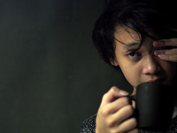 Portrait of boy holding coffee cup against black background