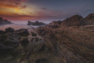 Scenic view of cliff by sea against sky during sunset