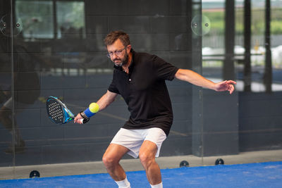 Man playing padel in a blue grass padel court indoor - young sporty boy padel player hitting ball 