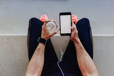 Low section of athlete using mobile phone while drinking water 