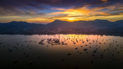 Flock of birds in sea against sky during sunset