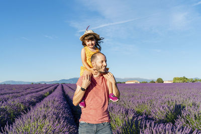 Father piggybacking little daughter in vast summer lavender field