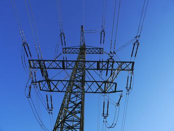 Low angle view of electricity pylon against clear blue sky