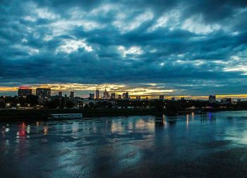View of city at waterfront against cloudy sky