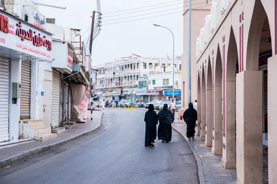 Rear view of people walking on road amidst buildings