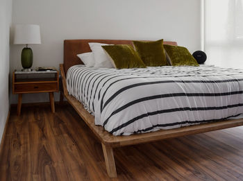 Bed base, bedroom with mat on the floor, clay pot in the background, wooden credenza and mirror.