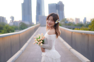 Portrait of smiling young woman standing against railing