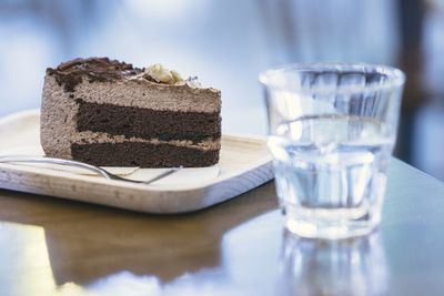 Close-up of cake slice in plate by drinking glass on table
