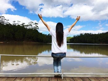 Rear view of woman standing by lake against sky