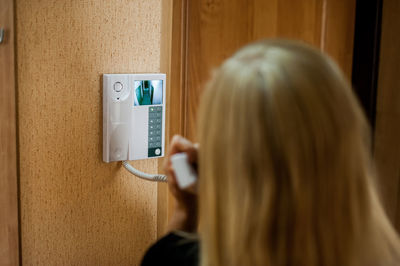 Rear view of woman using intercom at home