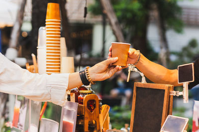 Man barista serving hot coffee in paper cup to customer over counter in cafe outdoor.