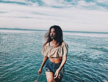 Young woman standing in sea against sky