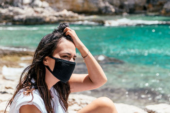 Portrait of a young woman wearing black protective mask on beach in summer. tourist, corona, covid.