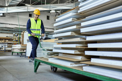 Worker pulling pallet jack with wooden boards in factory