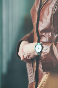 Midsection of woman wearing leather jacket and wristwatch while standing against blue wall