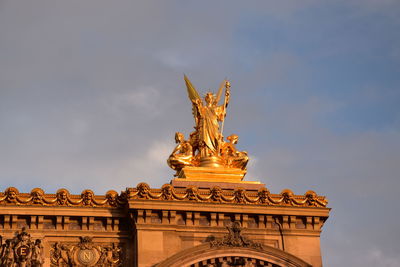 Low angle view of golden statue against cloudy sky